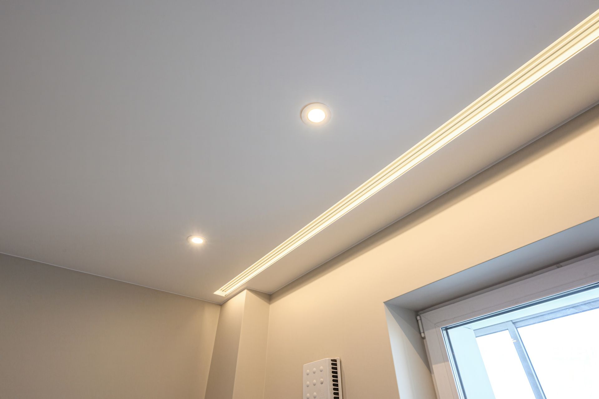 A room with a white-panelled ceiling, recessed spotlights & a linear LED strip along the perimeter.