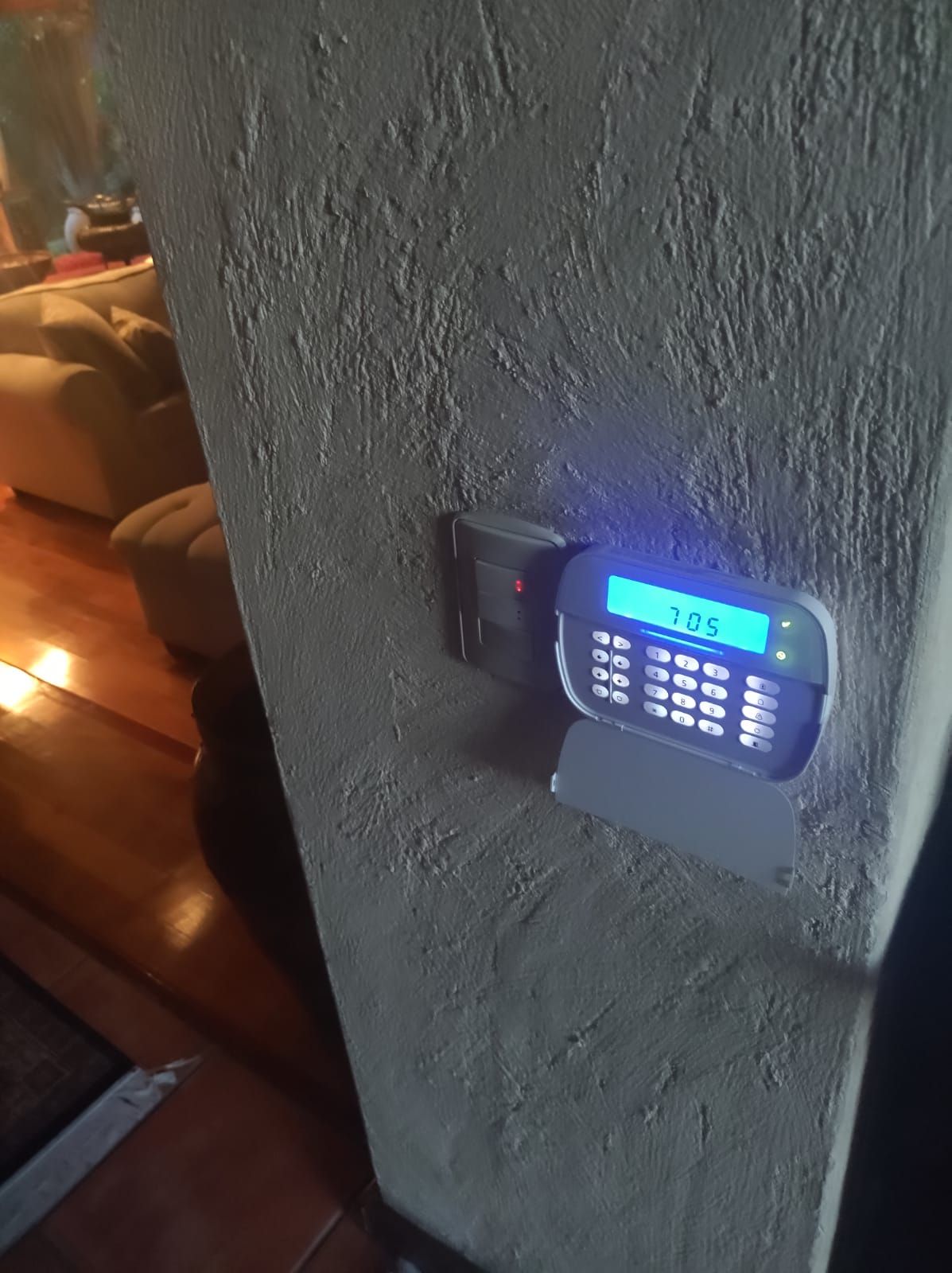 Teclado del sistema de seguridad montado en una pared gris texturizada. La pantalla muestra 