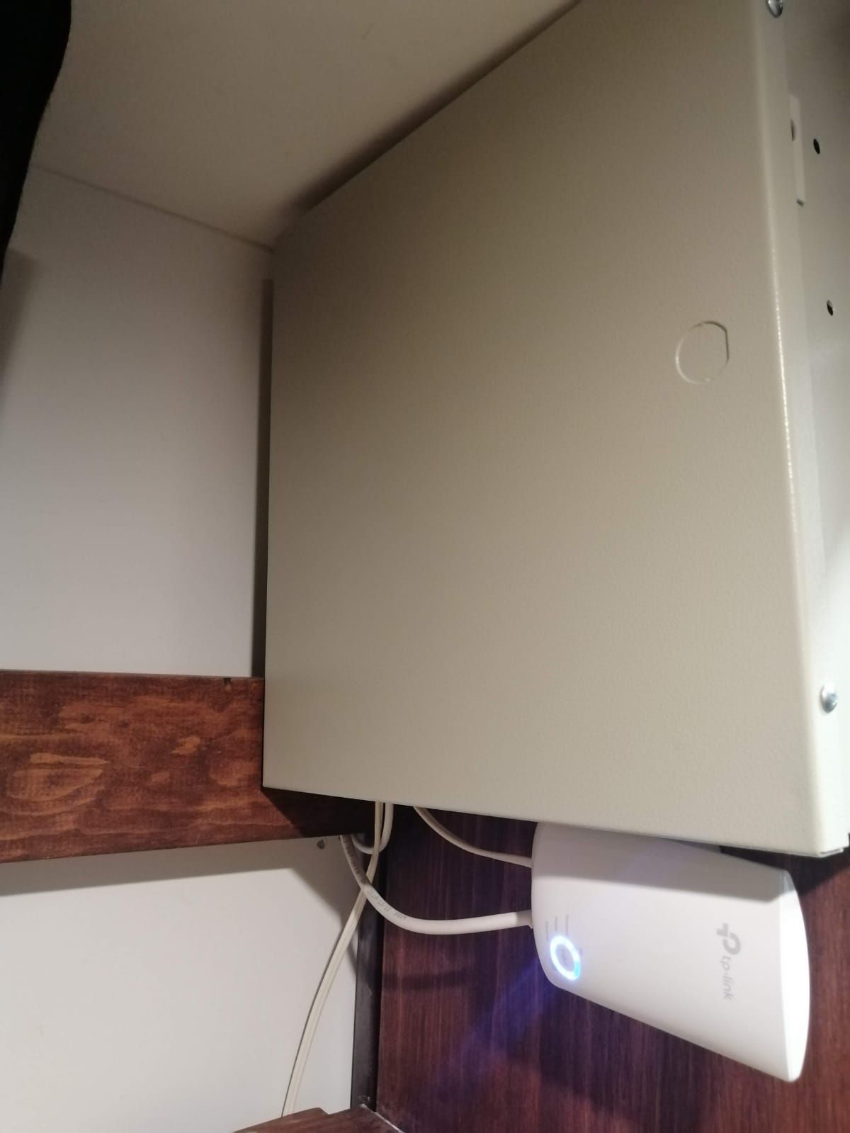 Caja de telecomunicaciones blanca montada sobre una superficie de madera con un dispositivo TP-Link blanco más pequeño debajo.
