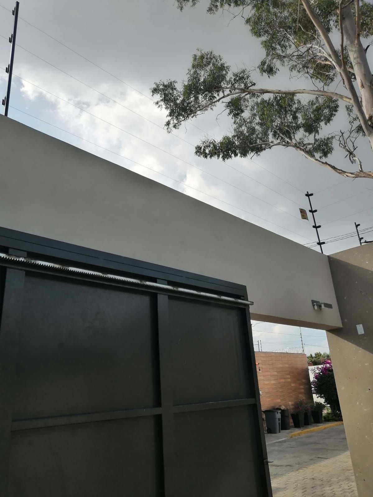 Puerta negra con valla de seguridad sobre un muro de hormigón bajo un cielo nublado.