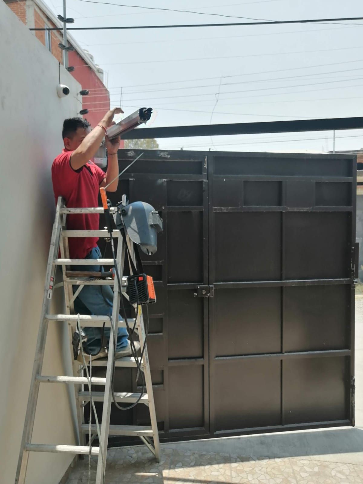 Hombre en una escalera instalando una cámara de seguridad encima de una puerta negra.