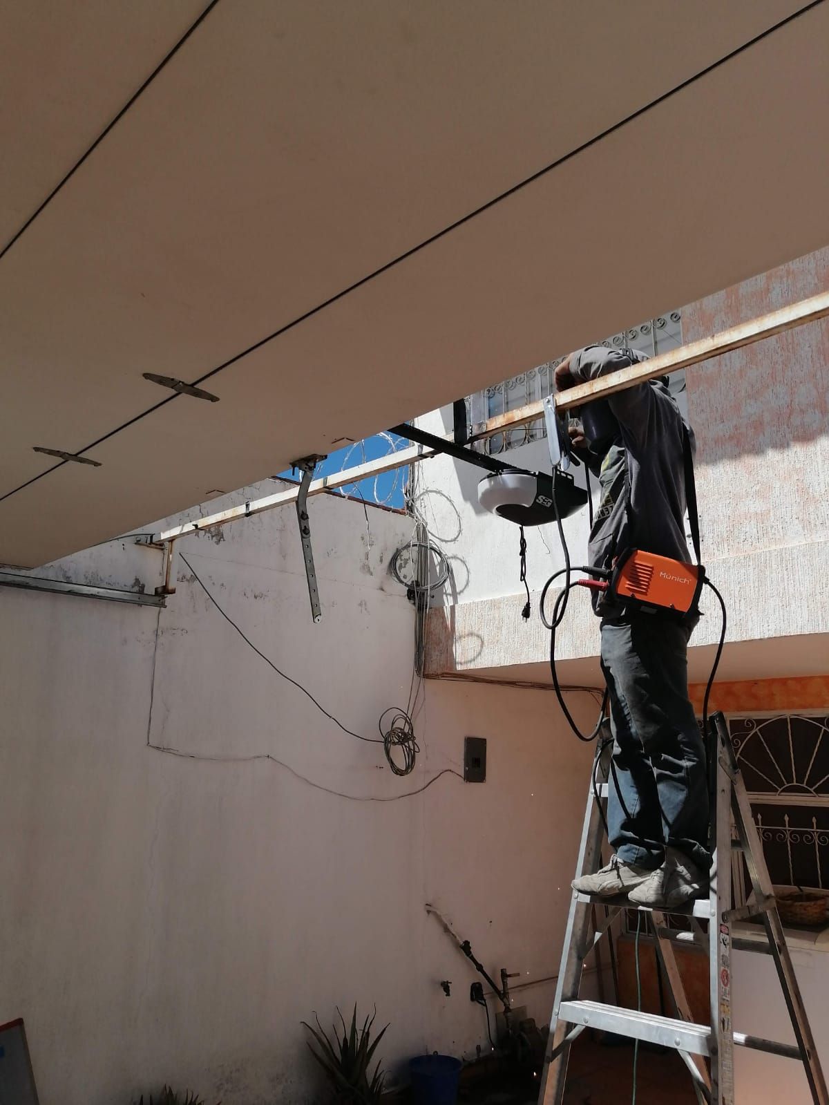 Soldador en una escalera trabajando en una estructura al aire libre. Lleva equipo de protección y equipo de soldadura.