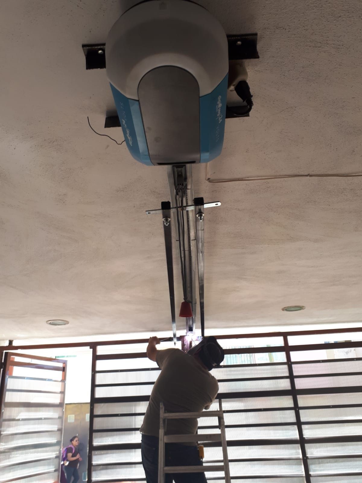 Hombre en una escalera instalando un abridor de puerta de garaje en un garaje.