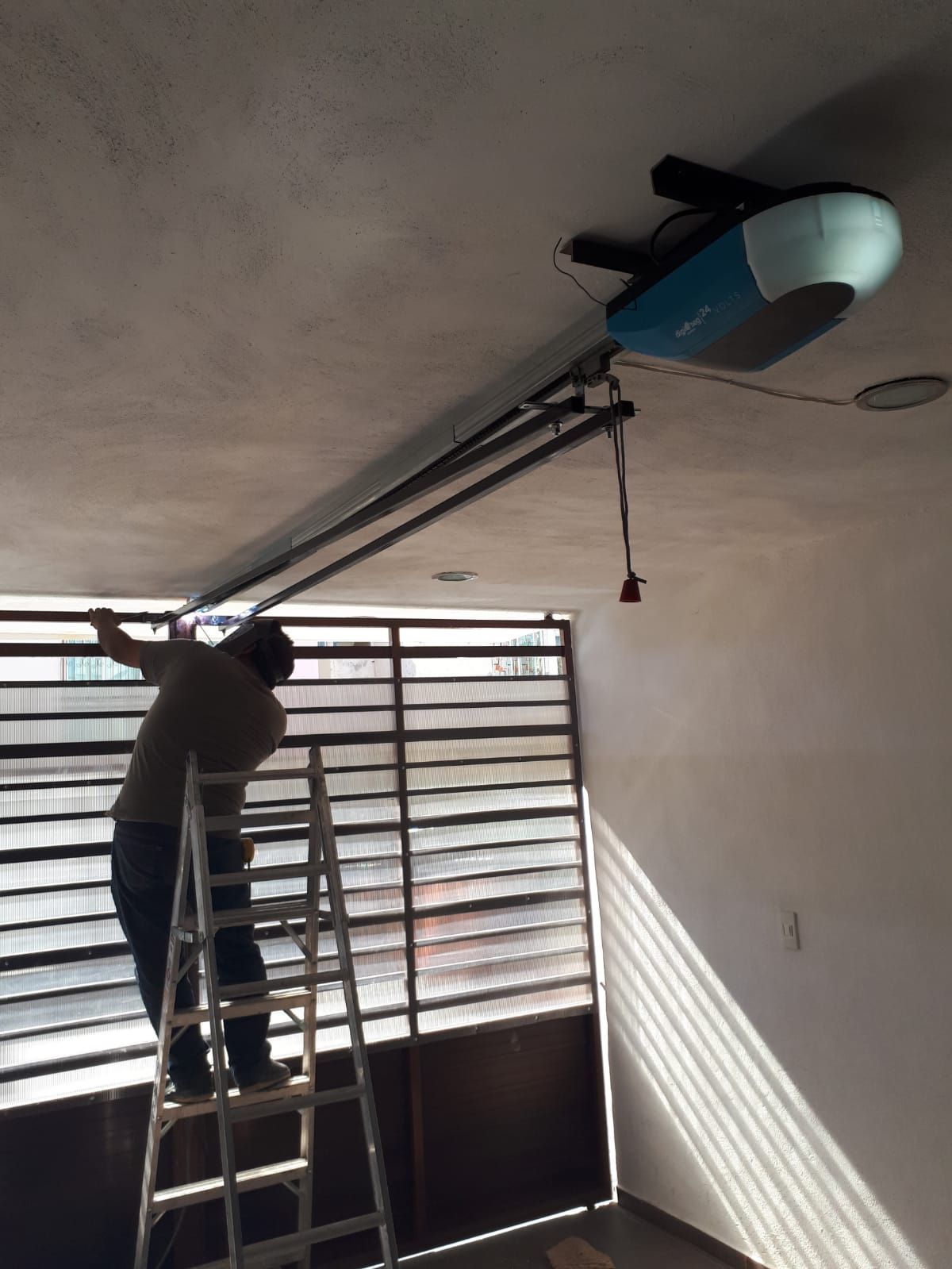Persona en una escalera instalando un abridor de puerta de garaje, en el interior.