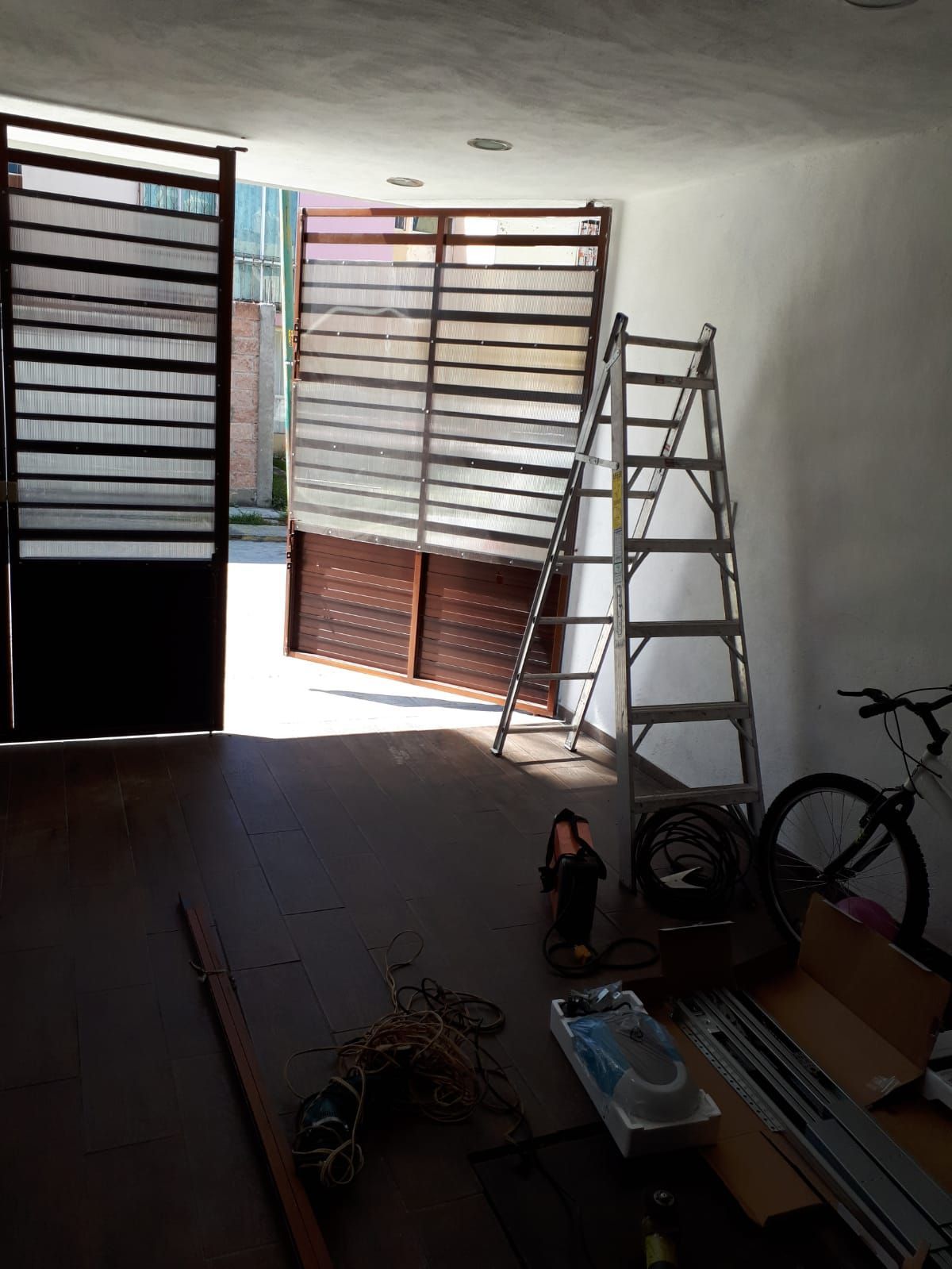 Garaje abierto con escalera apoyada en una puerta translúcida parcialmente levantada. Se ven herramientas y una bicicleta.