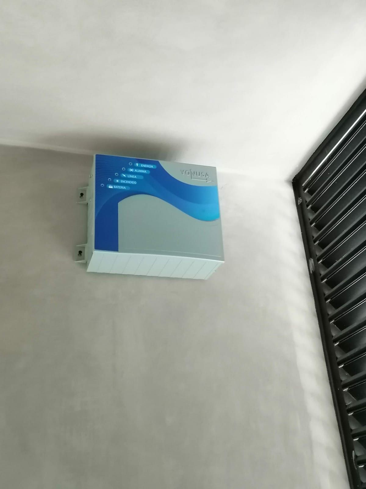 Dispositivo electrónico de color azul y gris montado en una pared de color gris claro, junto a una estructura enrejada de color negro.CEPROPUE