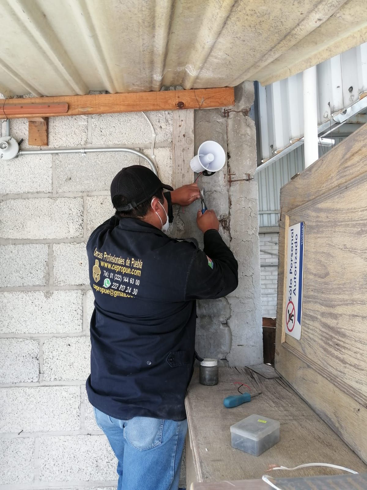 Hombre con ropa de trabajo instalando un altavoz blanco en una pared de hormigón.
