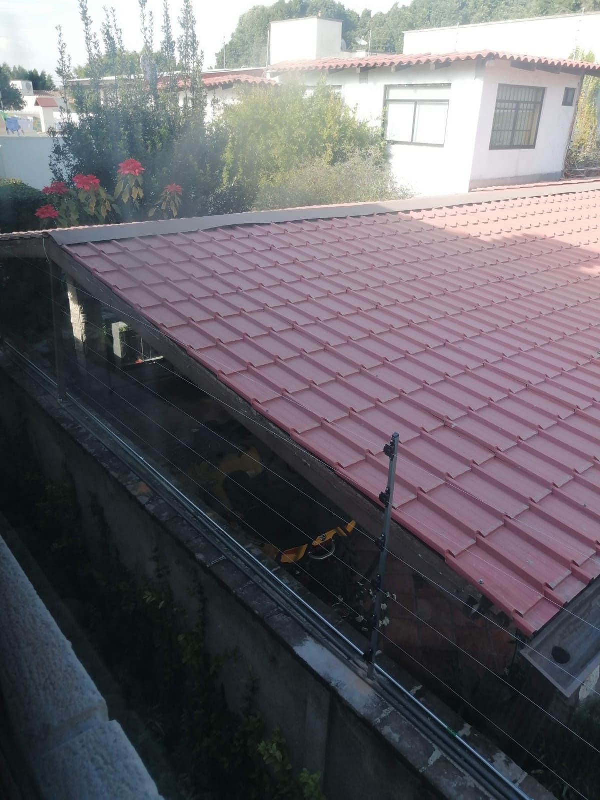 Techo de tejas rojas con valla de seguridad debajo, con vista a zona residencial en un día soleado.