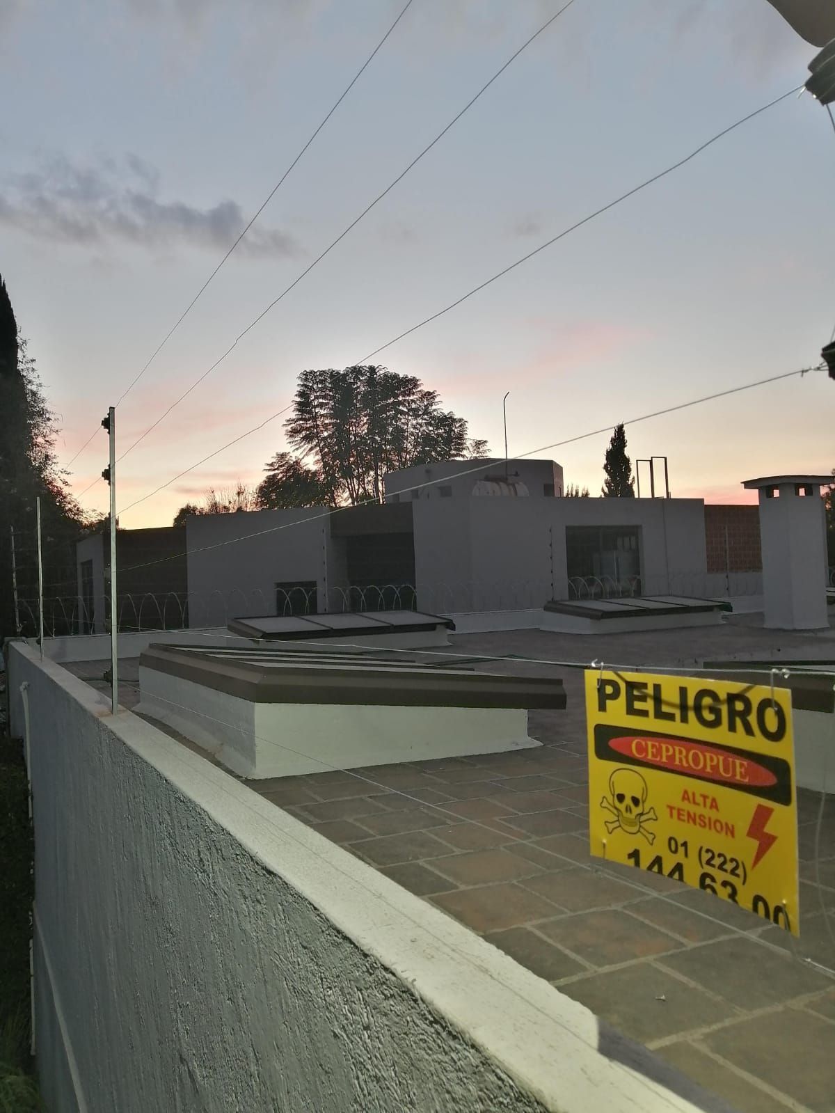 Azotea con valla de seguridad, señal de advertencia y una puesta de sol de fondo.