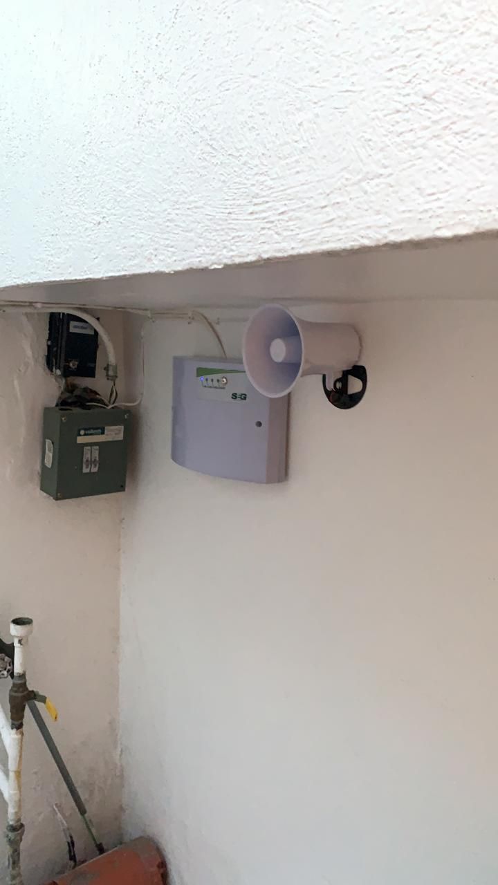 Pared blanca con sistema de seguridad: panel de alarma, sirena y cámara.