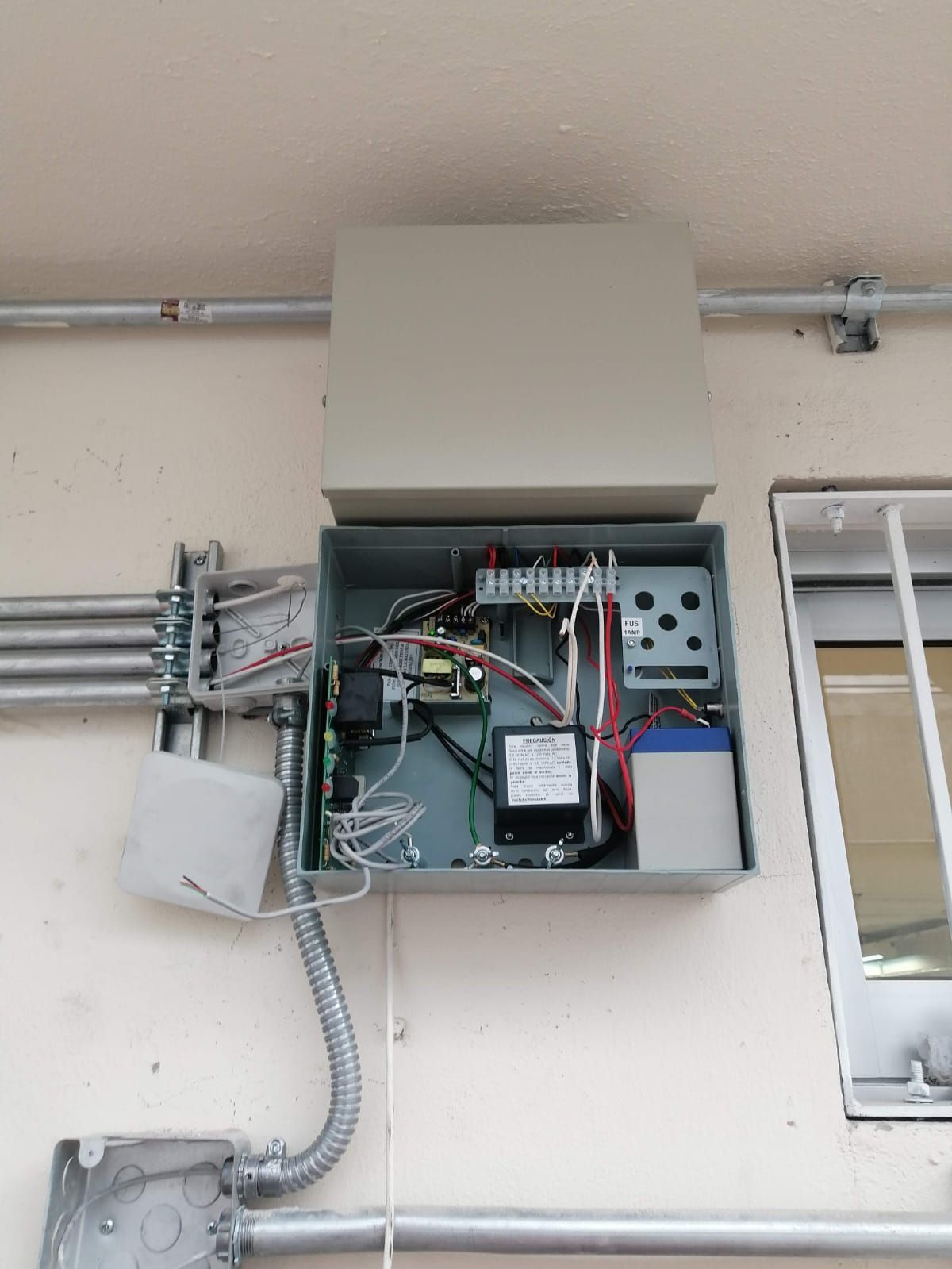 Caja eléctrica abierta en una pared, que contiene cableado, una batería y otros componentes.