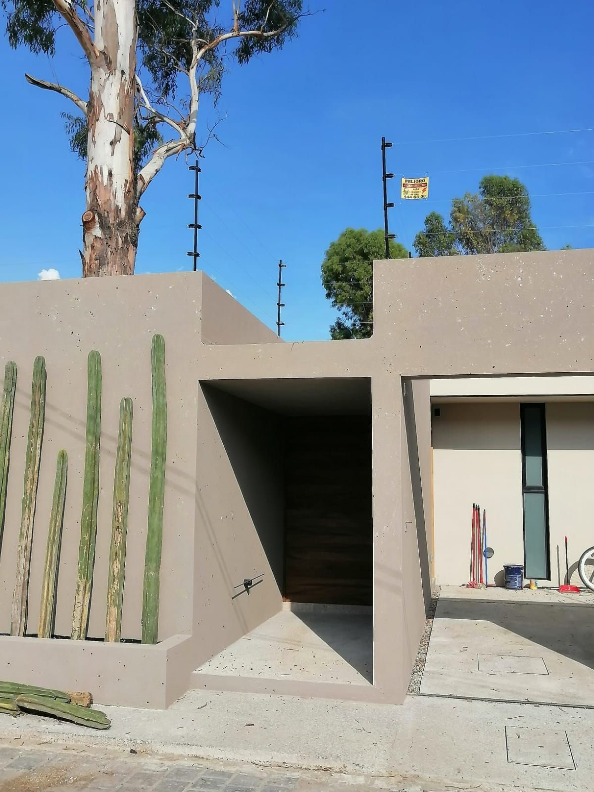 Edificio de estuco color canela con valla de seguridad, cactus y puerta en un día soleado.
