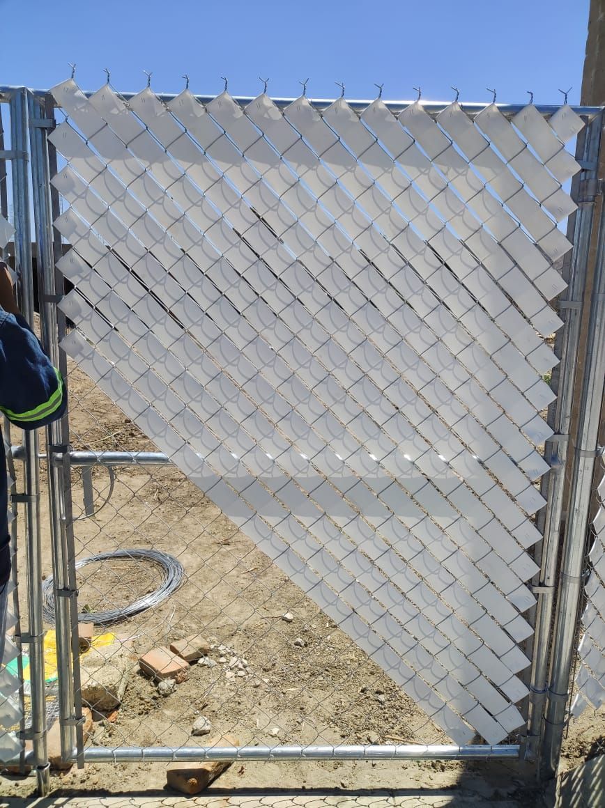 Valla de alambre con listones blancos para privacidad, parcialmente instalada, contra un cielo azul, en un sitio de construcción.