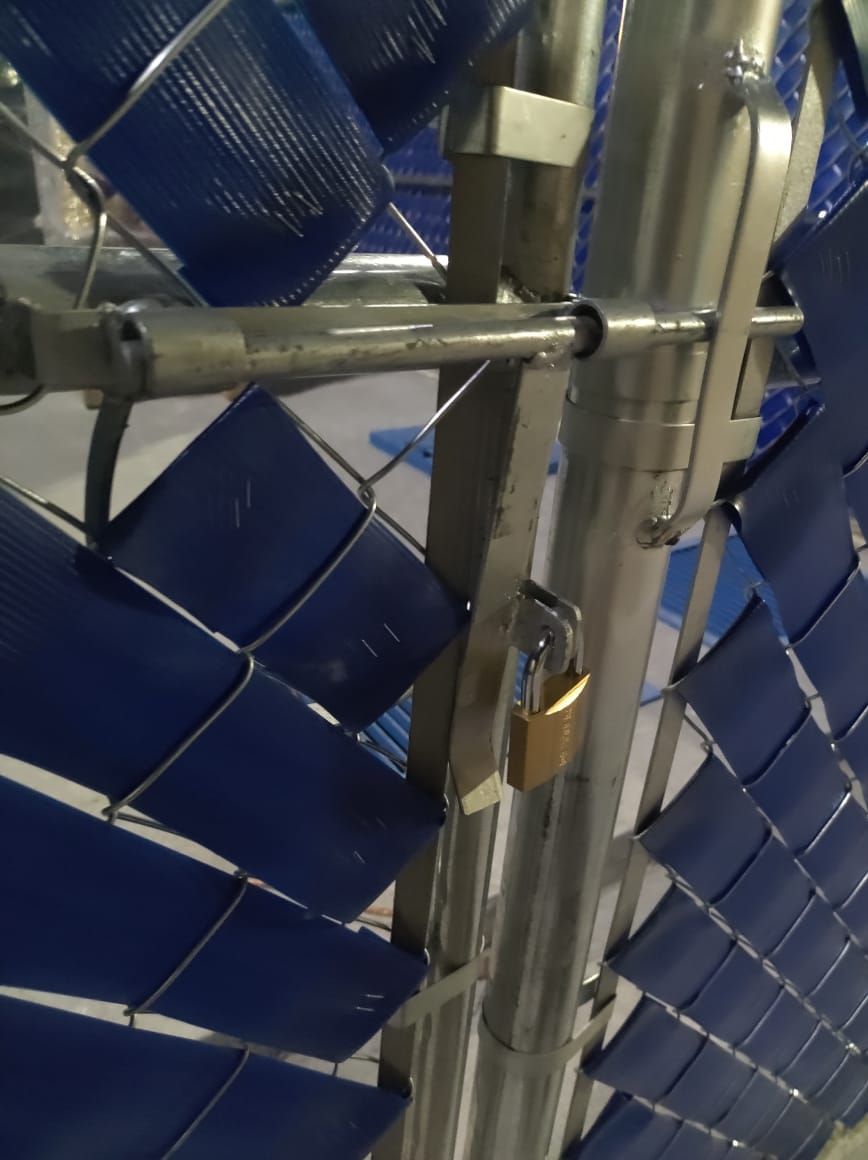 Una puerta de metal con un patrón tejido de color azul, asegurada con un candado.