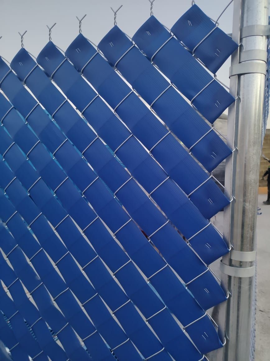 Listones azules tejidos a través de una valla de alambre, con un poste de metal a la derecha.