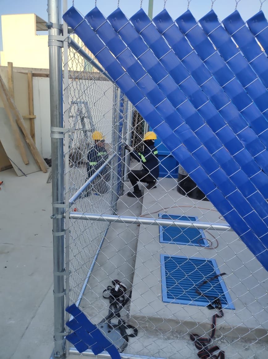 Trabajadores con chalecos de seguridad instalando vallas azules, cerca de hormigón, posiblemente en una obra en construcción.