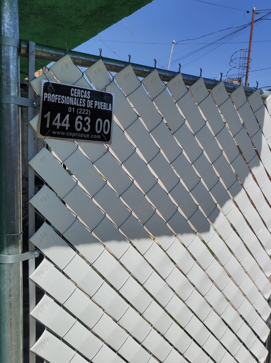 Un cartel negro con números y texto blancos cuelga de una valla de alambre blanca.