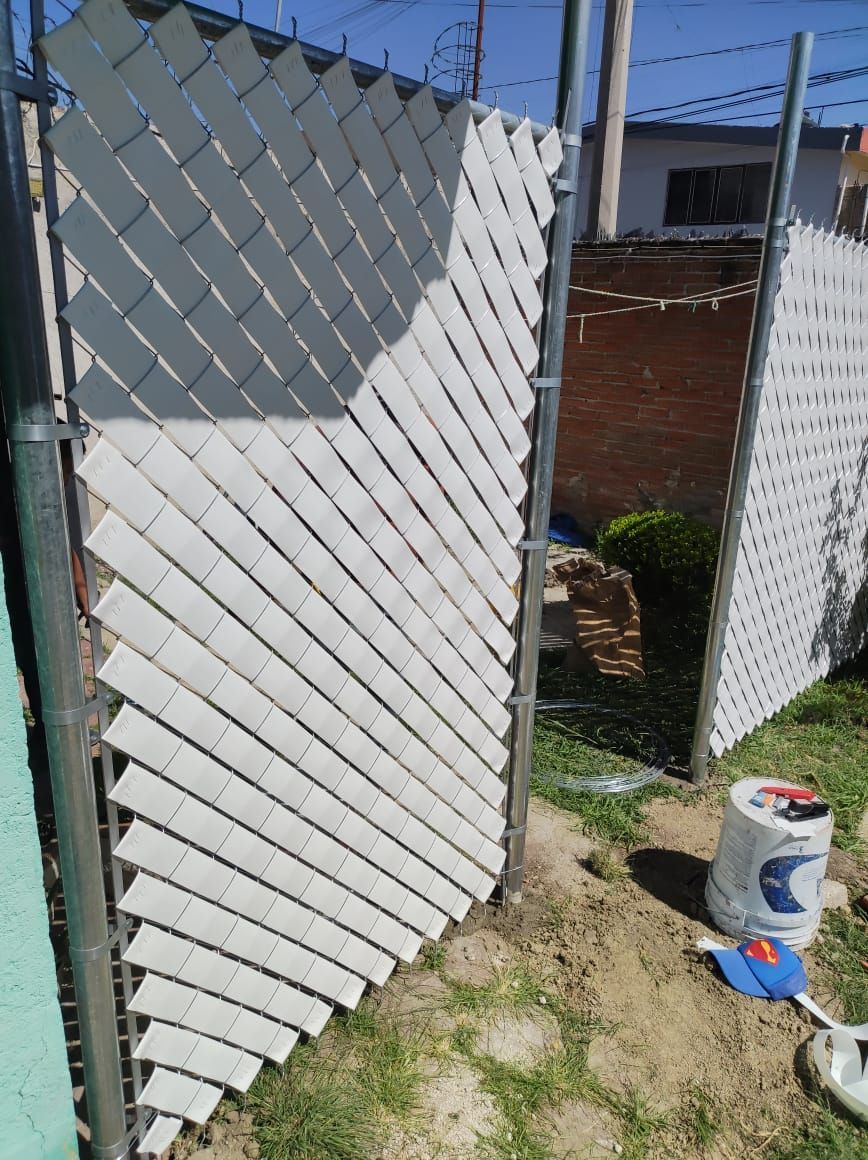 Tiras de vinilo blanco tejidas a través de una cerca de alambre, formando un patrón diagonal.