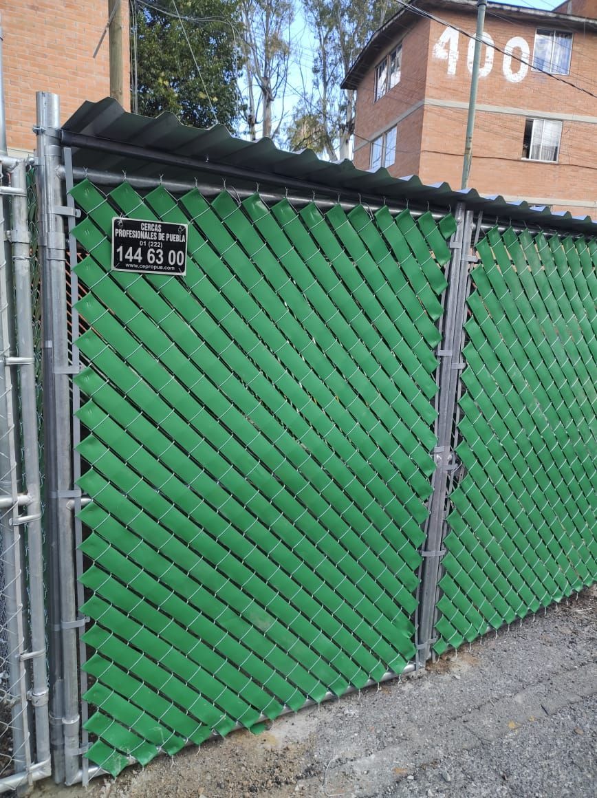 Valla verde de privacidad con portón, junto a edificio con el número 400.