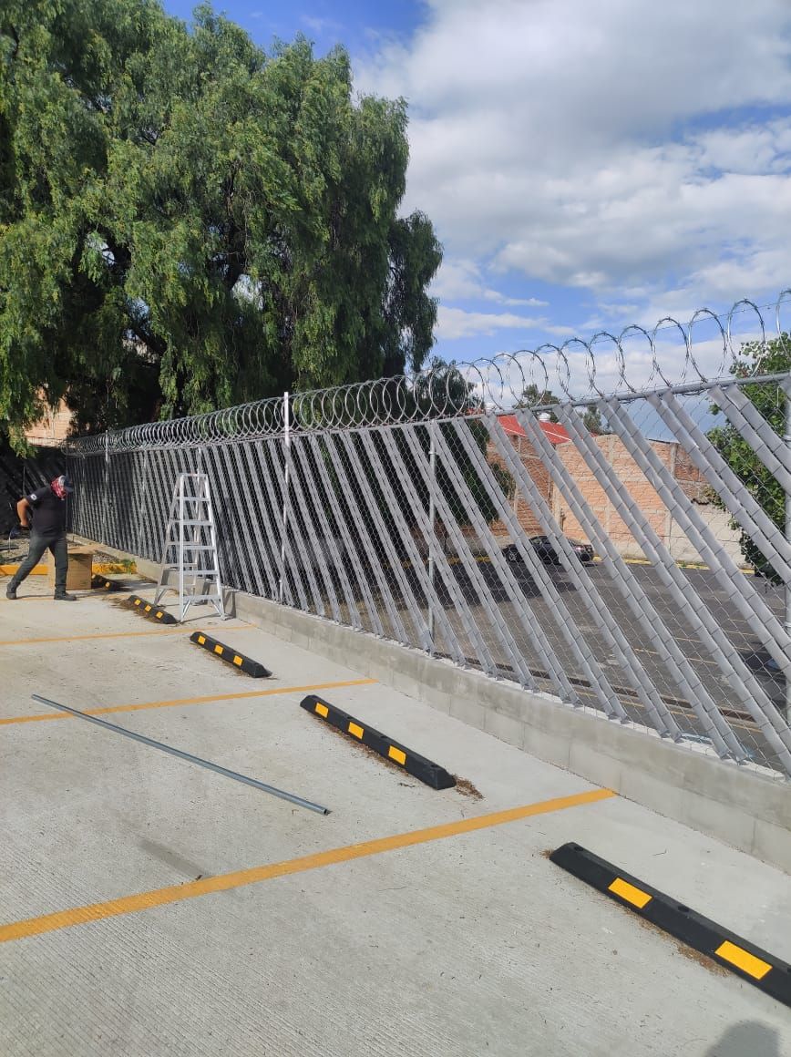 Hombre instalando una valla de seguridad con alambre de púas en un estacionamiento en un día soleado.