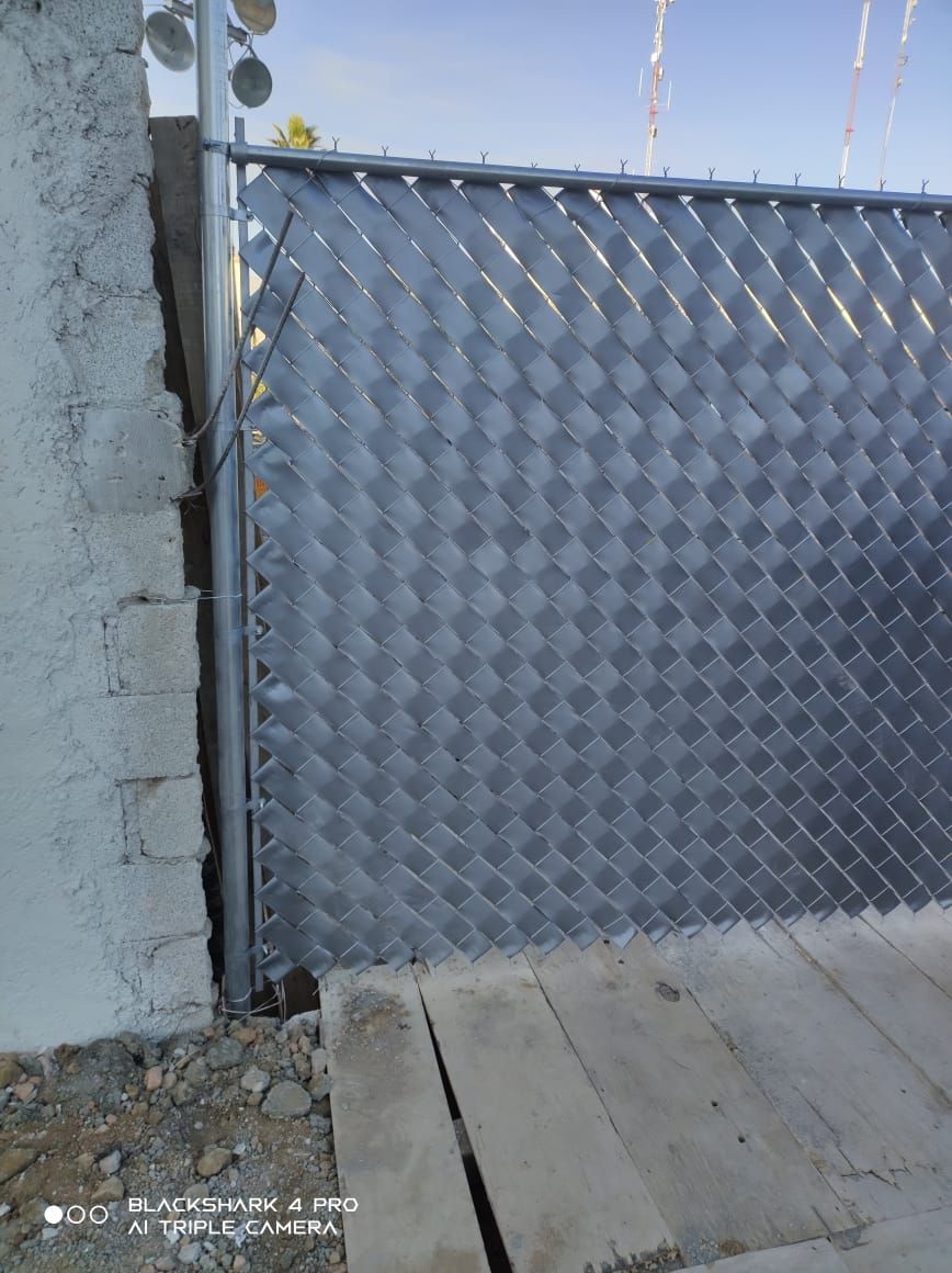 Cerca de alambre de metal con cubierta en forma de diamante, adyacente a un muro de concreto y un camino.