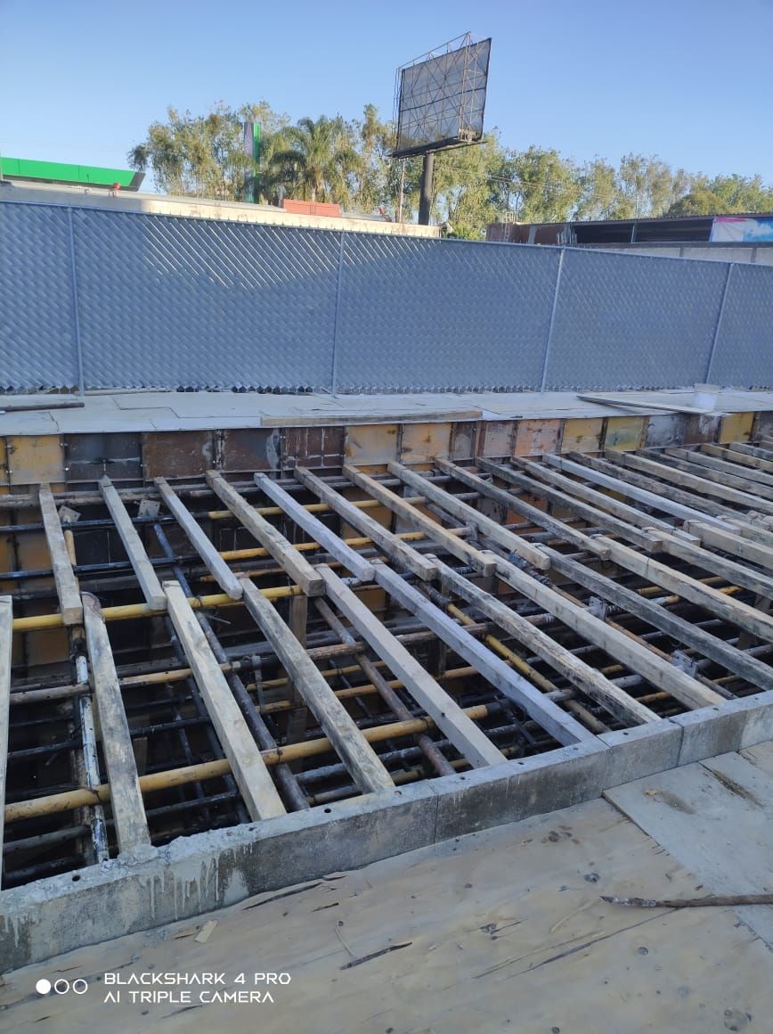 Obra con estructura de madera y varillas de refuerzo, lista para hormigonar. Entorno soleado al aire libre.