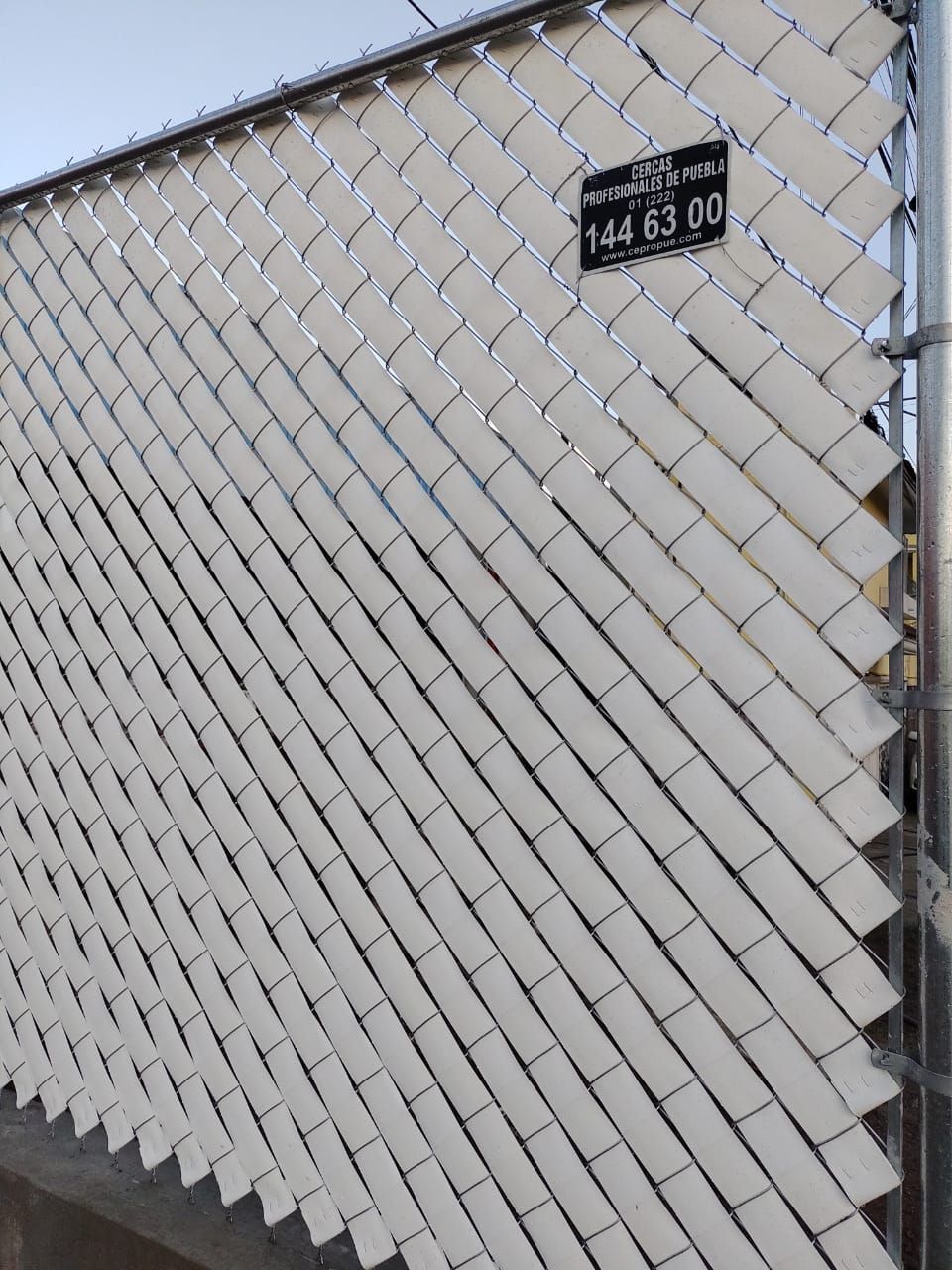 Cerca de alambre con listones blancos y un cartel negro que dice 