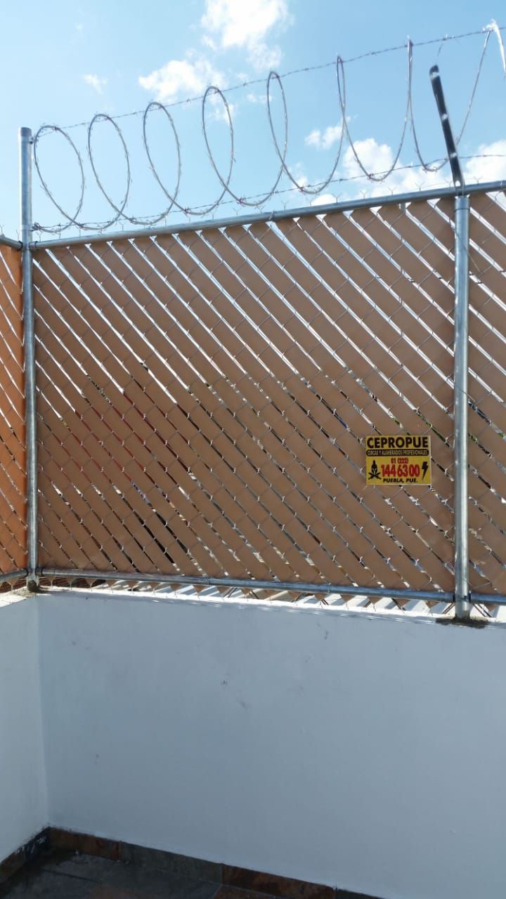 Valla de seguridad marrón y blanca con alambre de púas, contra un cielo azul.