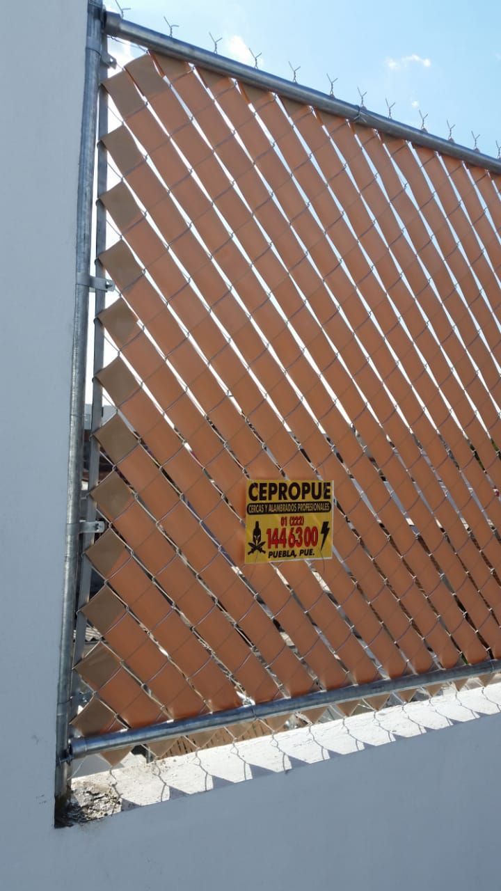 Valla de privacidad diagonal de color tostado con letrero, adherida a un edificio.