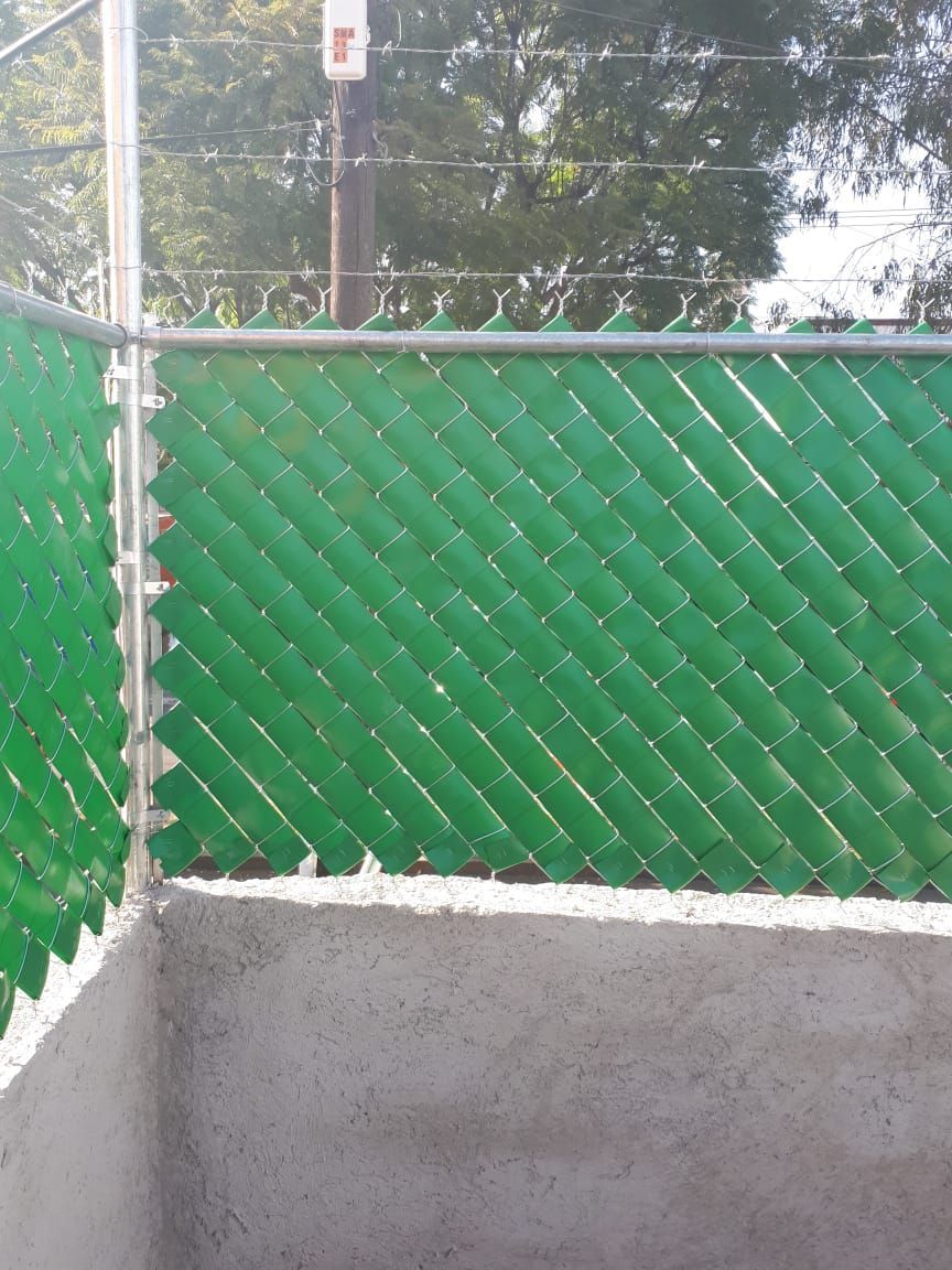 Botellas de plástico verdes tejidas para formar una valla de alambre; pared de hormigón gris en primer plano.