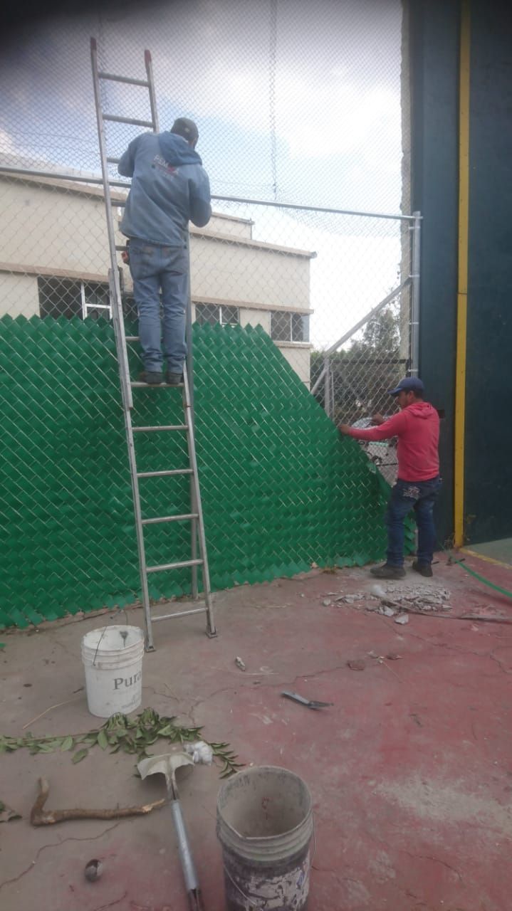 Dos personas instalando una valla de plástico verde a lo largo de una valla de alambre.