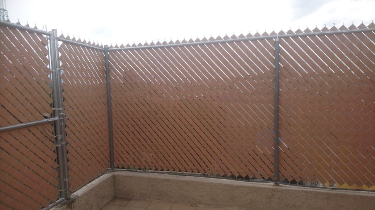 Listones marrones para privacidad tejidos en una cerca de alambre, creando un recinto de esquina.