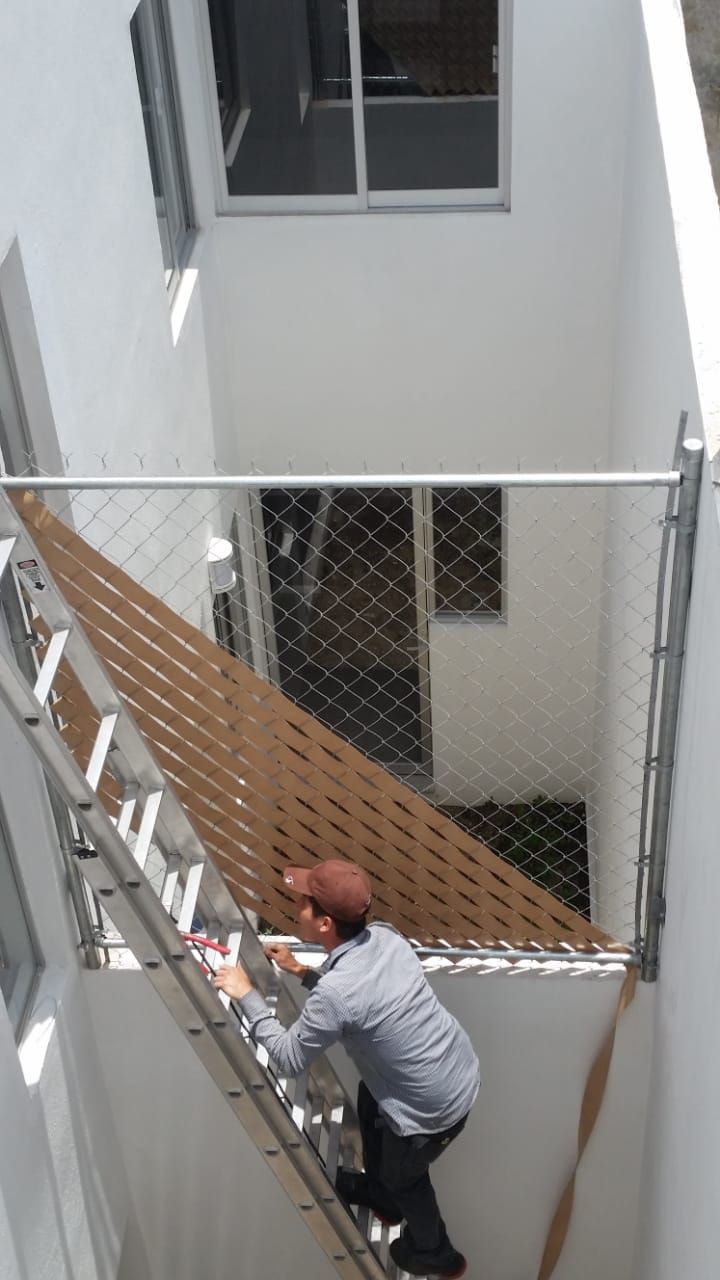 Hombre en una escalera, instalando un panel de valla marrón entre edificios blancos.