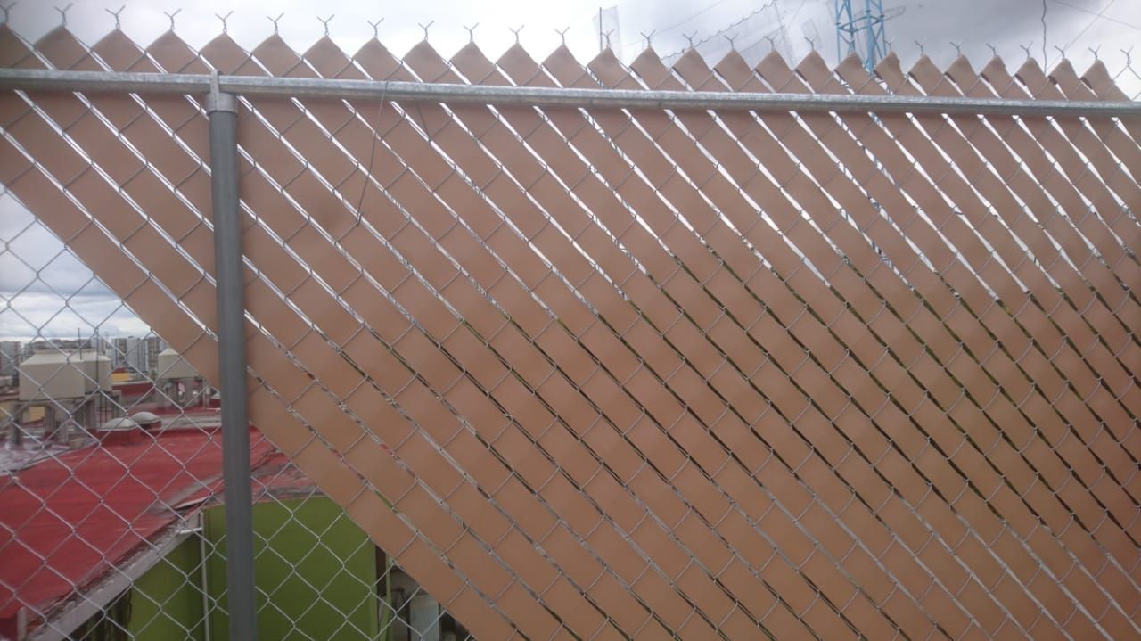 Listones marrones para privacidad tejidos en una cerca de alambre, que ocultan la vista de la azotea.