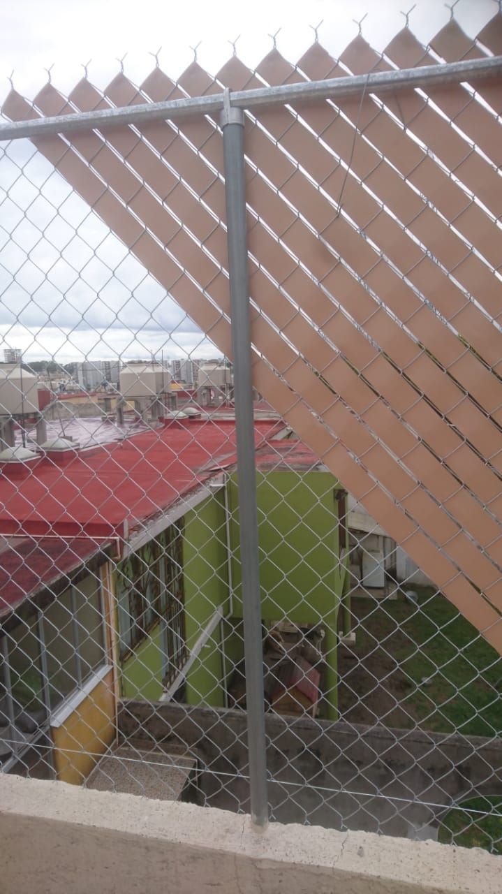 Valla de alambre con listones marrones para privacidad, edificios de la ciudad al fondo.