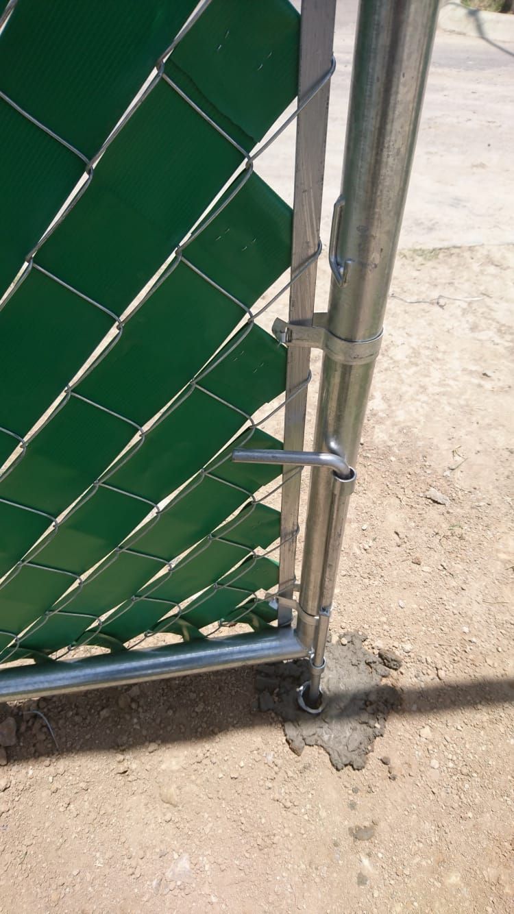 Una puerta de valla de alambre de cadena verde con listones para privacidad, asegurada con un pestillo, colocada en hormigón.