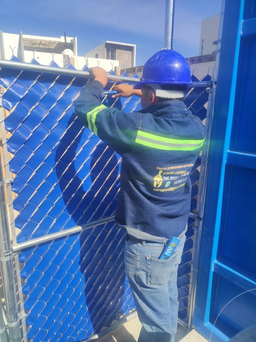 Trabajador con uniforme azul instalando paneles azules en una estructura metálica. Al aire libre, soleado.