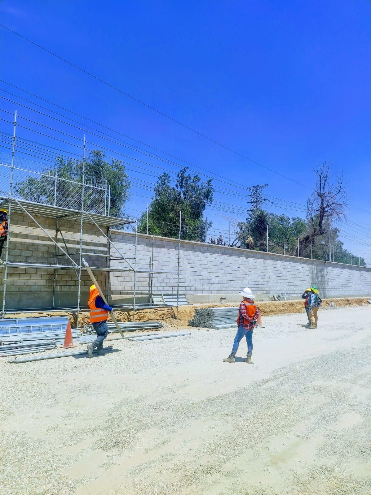 Obreros de la construcción en un camino de tierra, construyendo un muro de hormigón bajo un cielo azul.