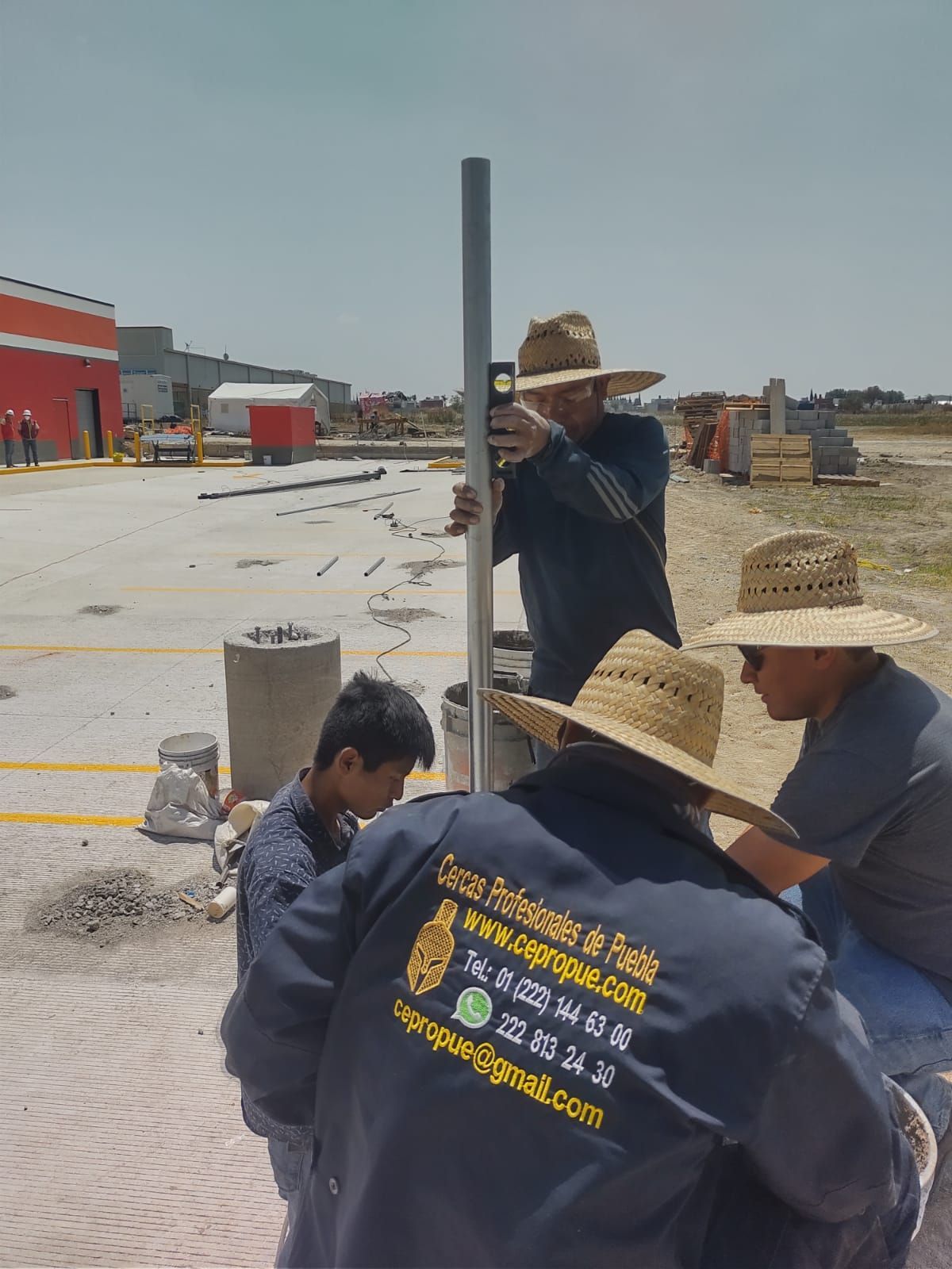 Obreros de la construcción instalan un poste metálico al aire libre con herramientas. Un trabajador lo comprueba con un nivel.