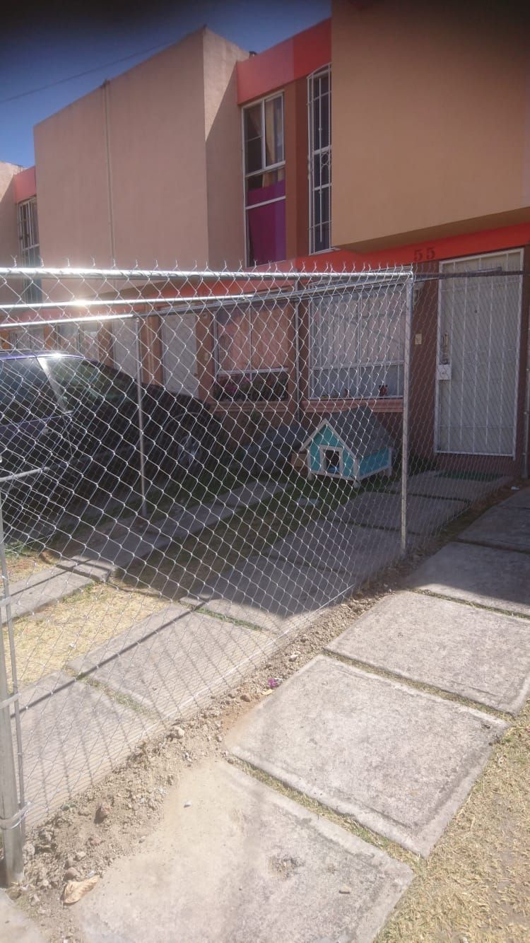 Una casa cercada por fuera con un coche aparcado dentro. Hay una caseta para perros junto a la casa.