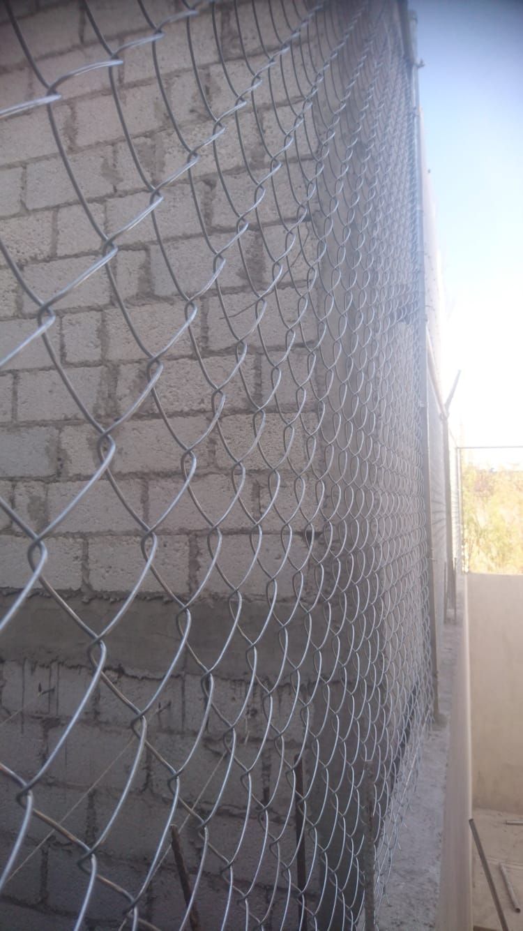 Valla de alambre delante de una pared de ladrillos.