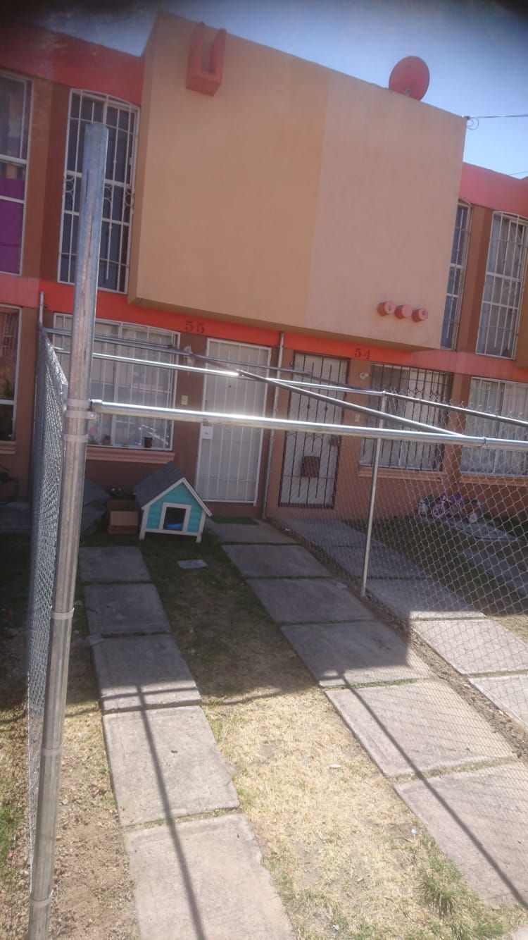 Casa naranja y blanca de dos pisos con caseta para perros azul claro al frente. Entrada de concreto y cerca metálica.