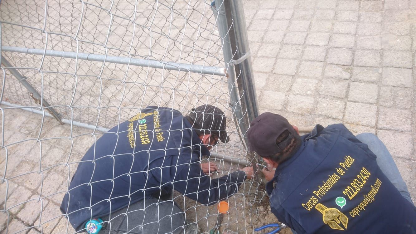 Dos trabajadores con chaquetas azules arreglando una valla de alambre.