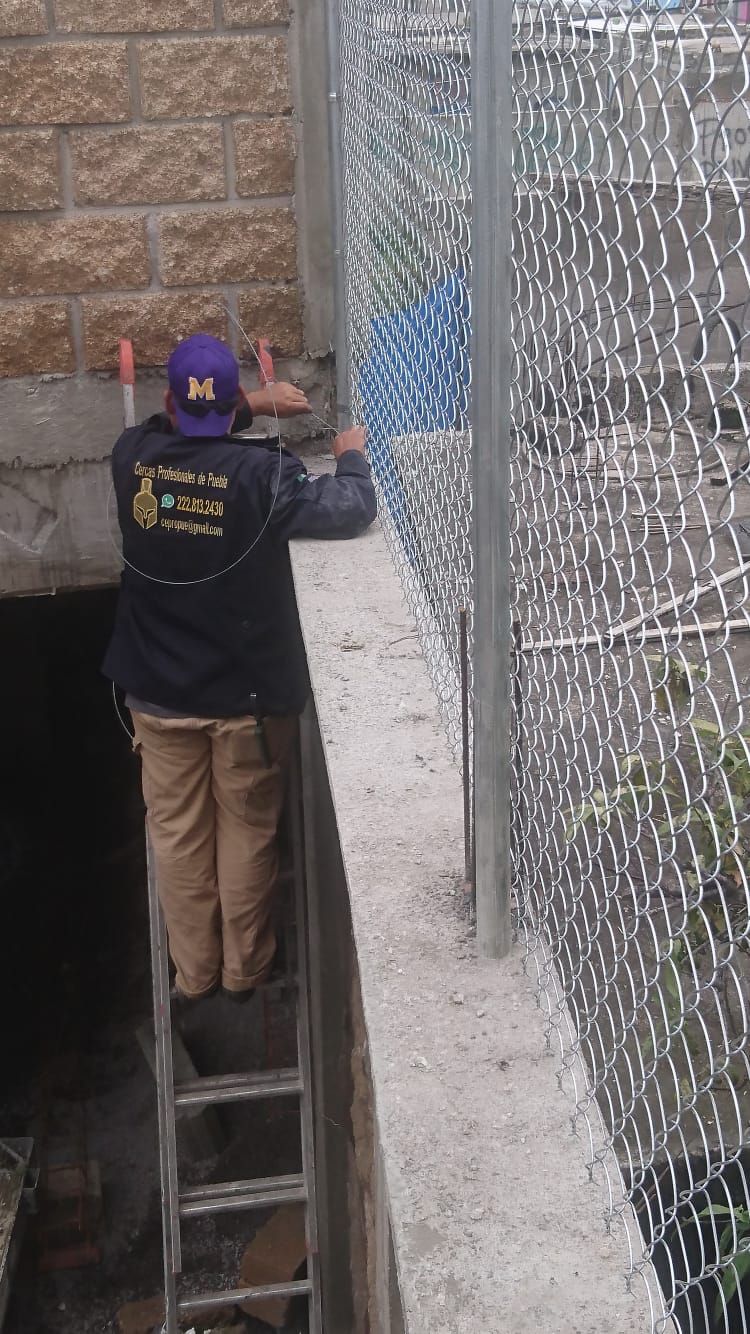 Persona en escalera instalando una valla de alambre contra un muro de piedra.