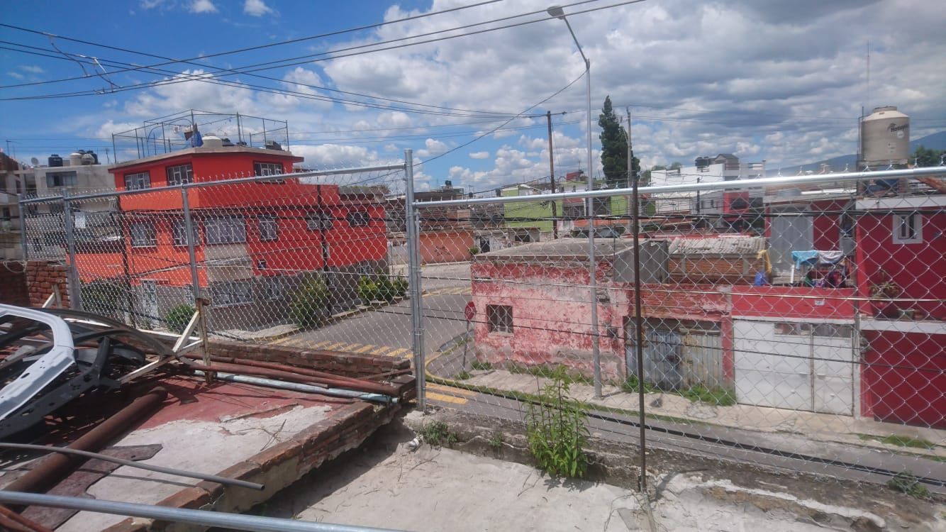 Valla de alambre frente a una zona residencial con edificios coloridos bajo un cielo nublado.