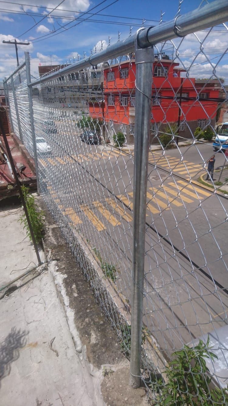 Valla de alambre en un tejado con vistas a una calle con coches y un edificio rojo.