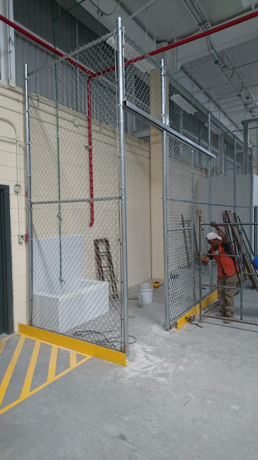 Un trabajador instala una cerca de alambre dentro de un edificio. En primer plano se ven marcas amarillas y negras en el suelo.
