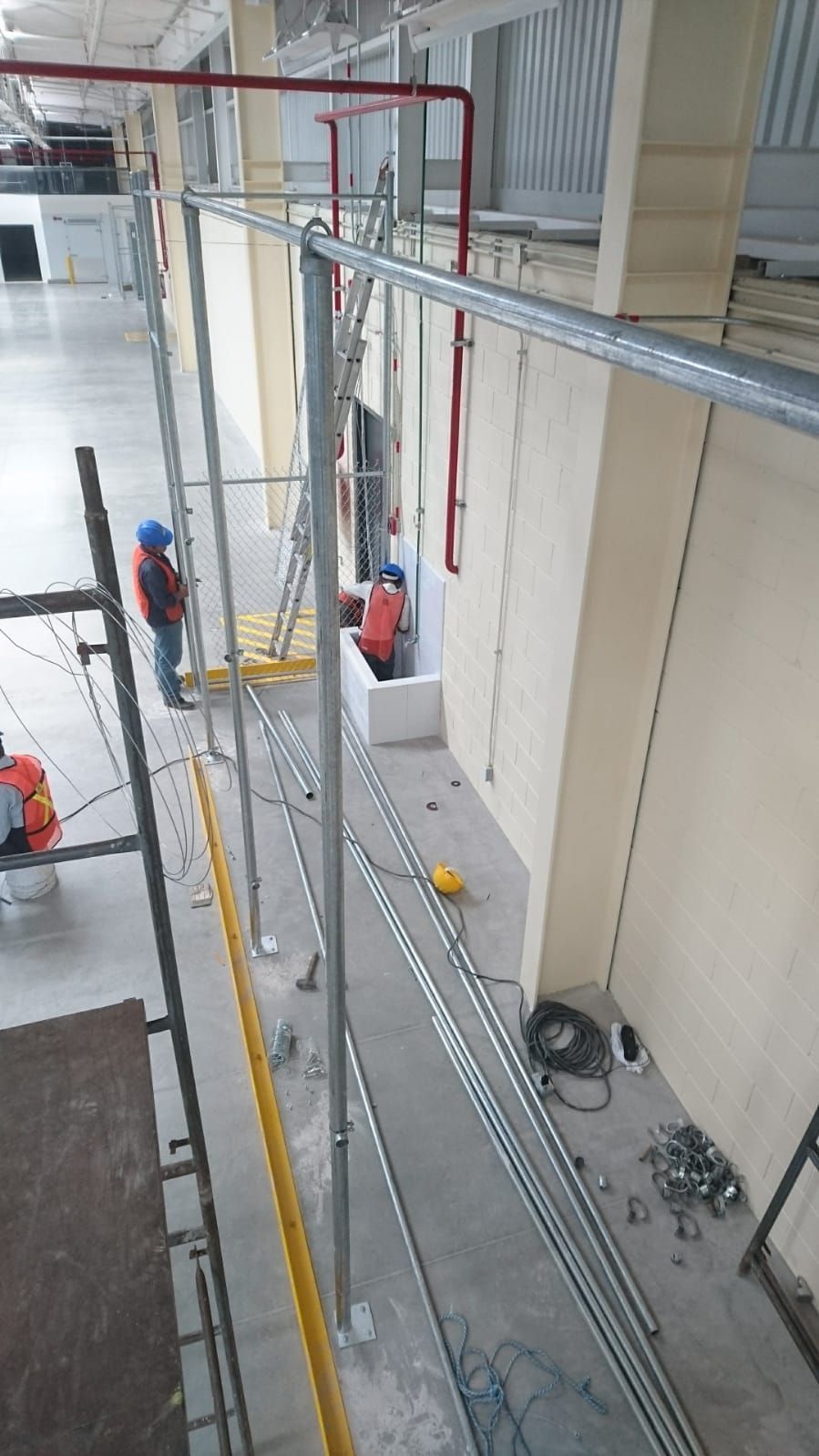 Los trabajadores de la construcción instalan tuberías de metal a lo largo de una pared de un edificio.