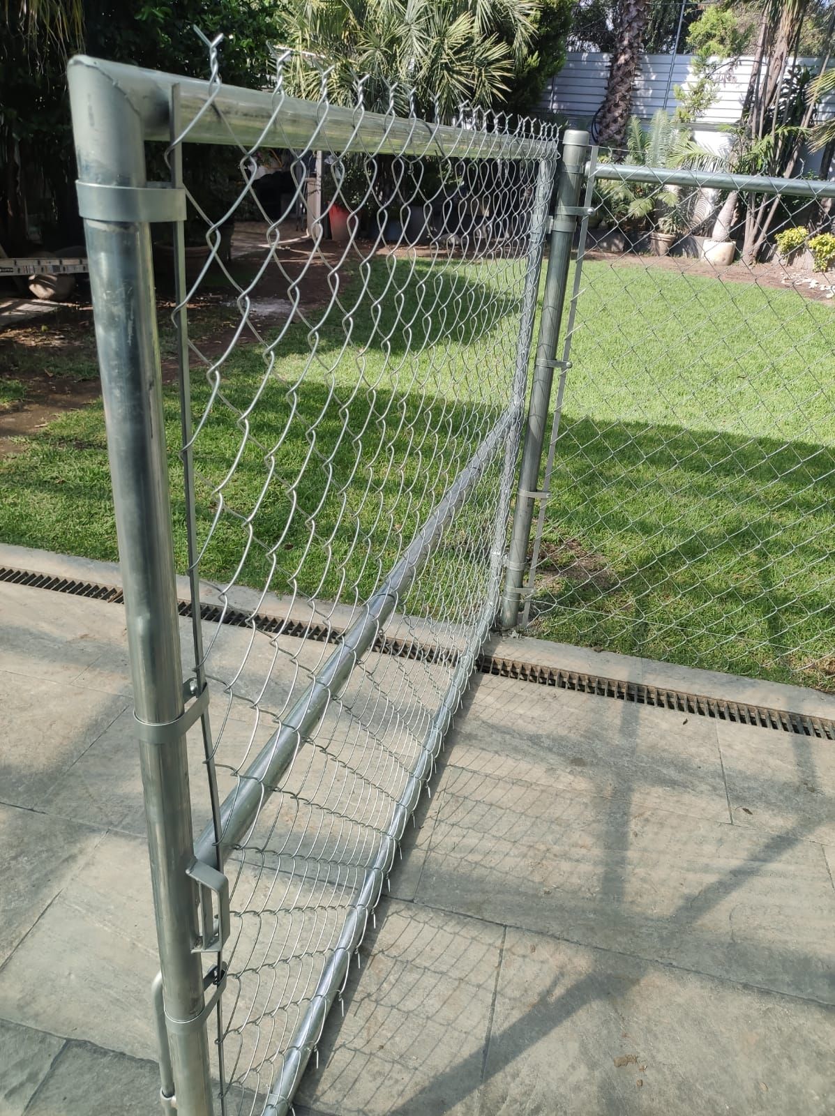 Puerta de alambre en un patio con césped, al lado de un patio de piedra.