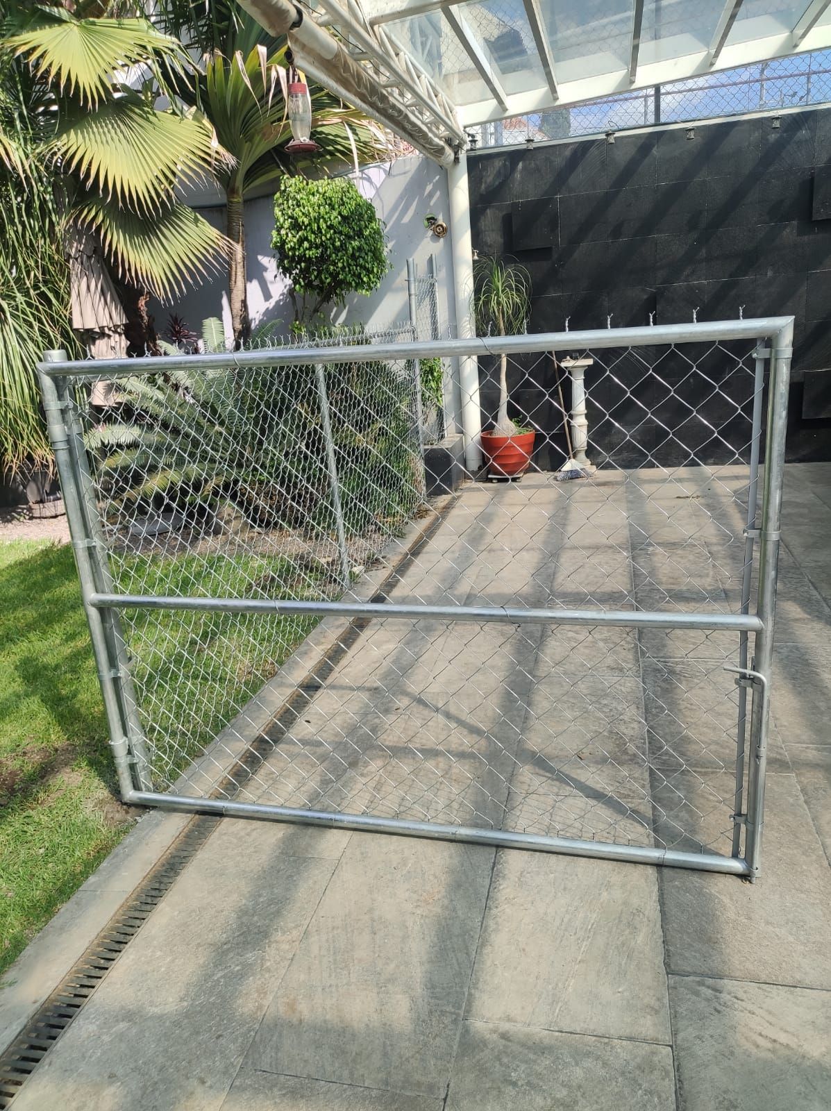 Puerta de valla de alambre de cadena en un camino de entrada de hormigón, frente a una casa con puerta.
